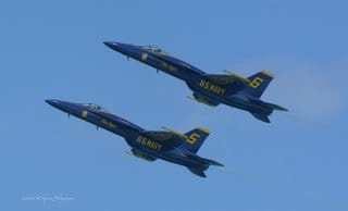 Two Blue Angels jets fly together across a clear blue sky. — by Ed Shpritz