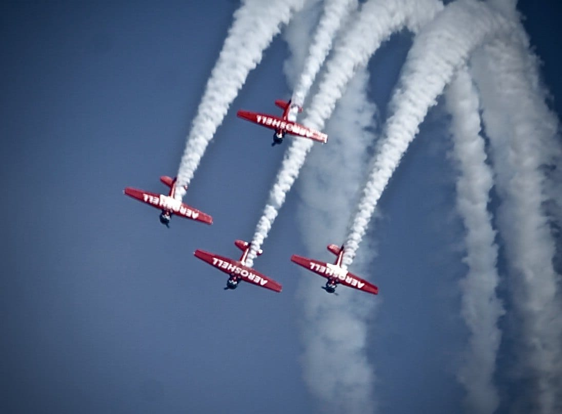 Four red aircraft leave parallel smoke trails overhead. — by Ed Shpritz