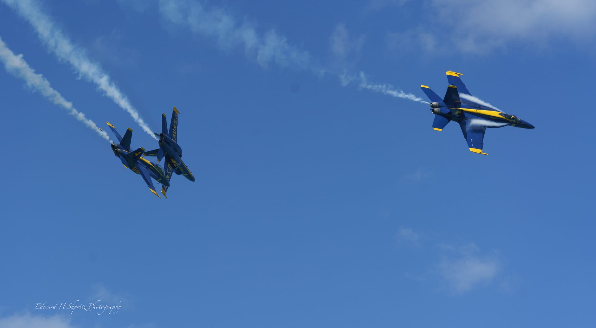 Two jets separate across the sky with smoke trailing behind. — by Ed Shpritz