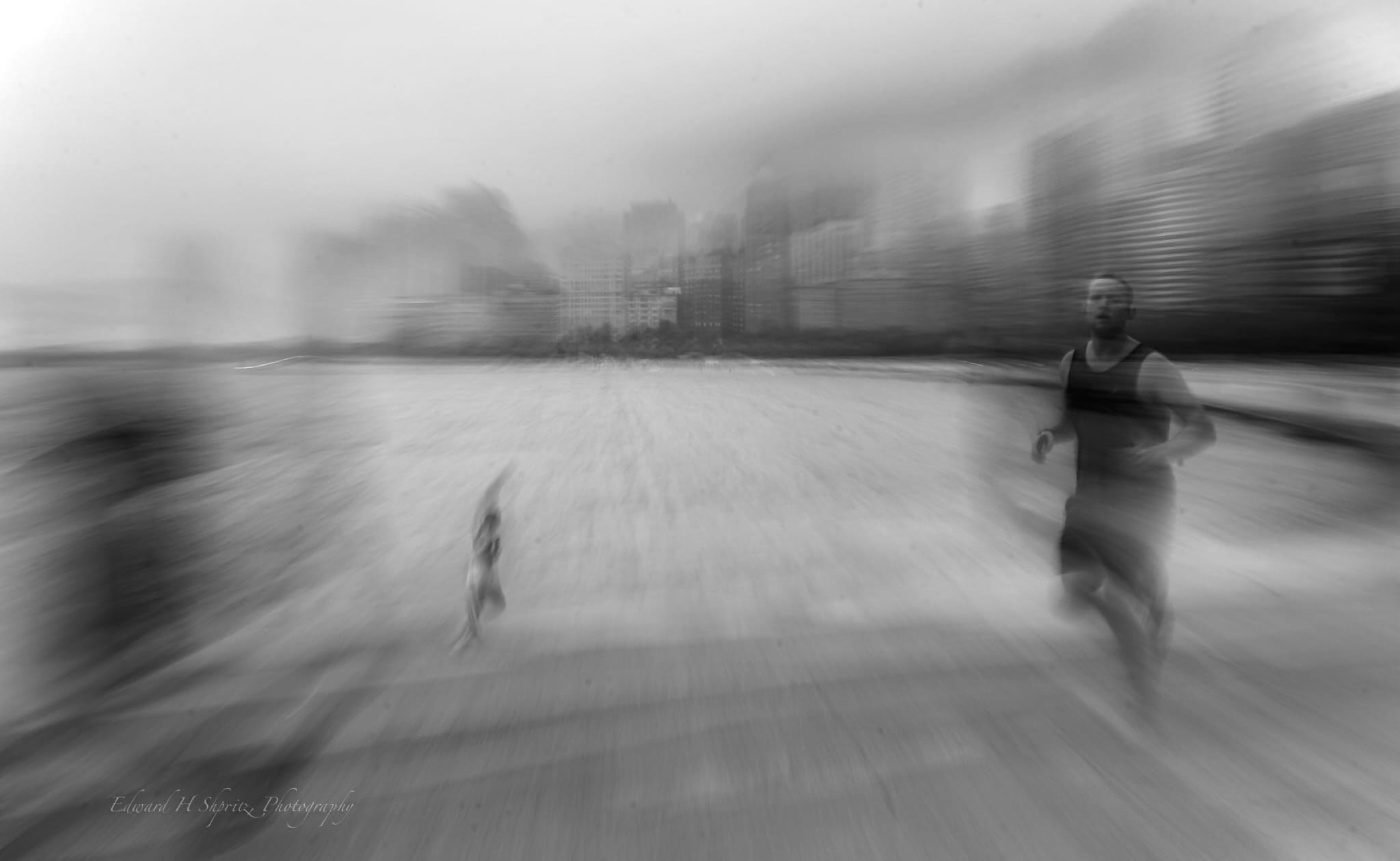 A runner crossing a beach as the shoreline and city dissolve into black-and-white motion