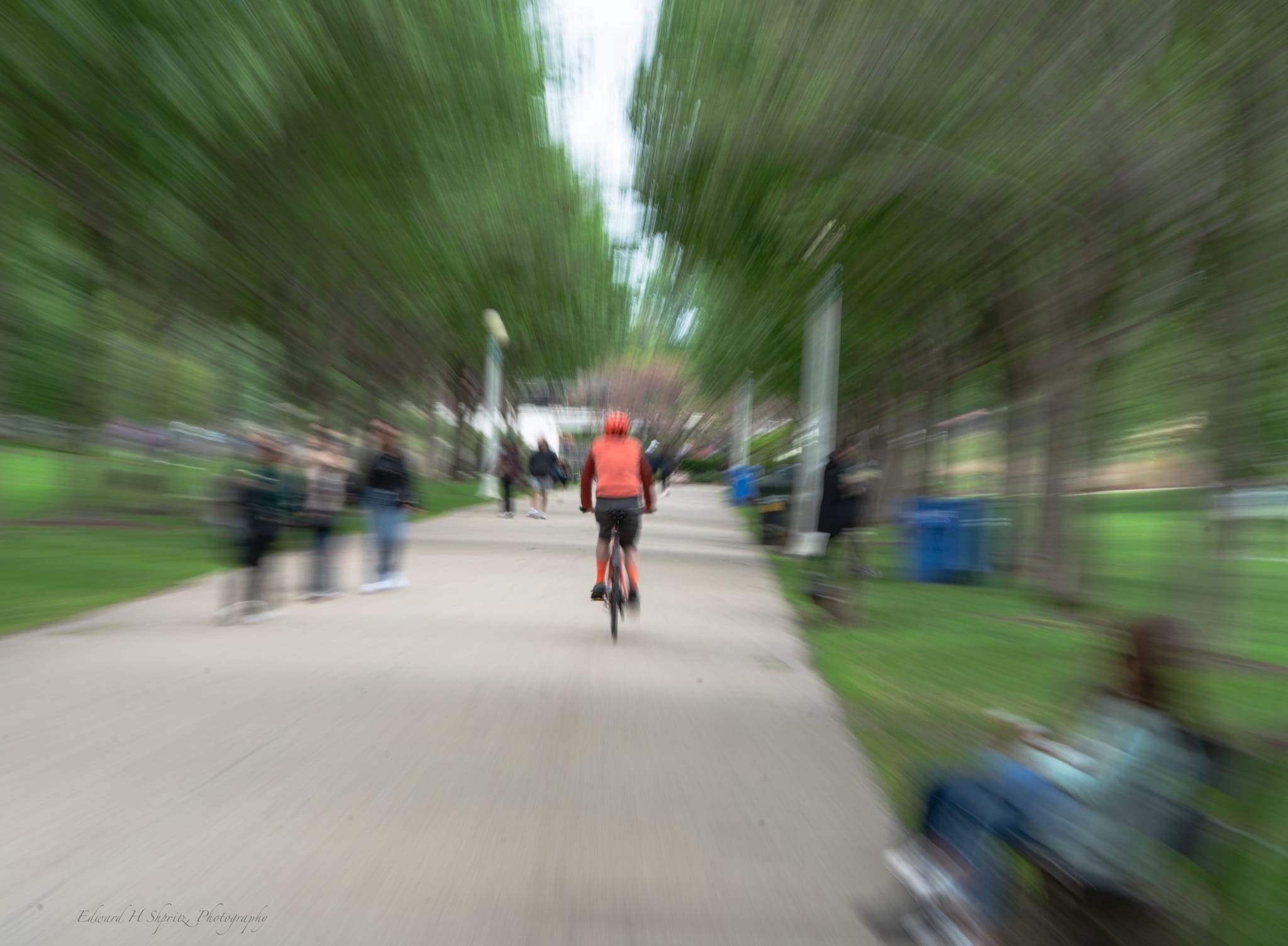 A cyclist in red riding through a park as the surroundings rush outward