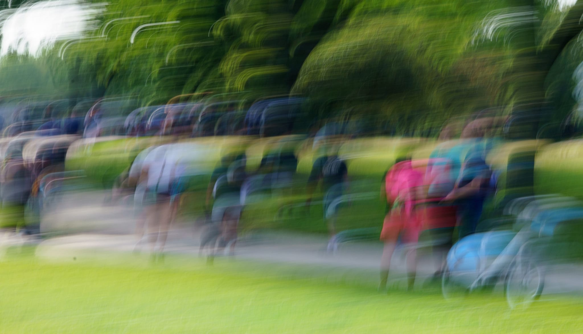 A procession of people repeated by motion across a bright green park