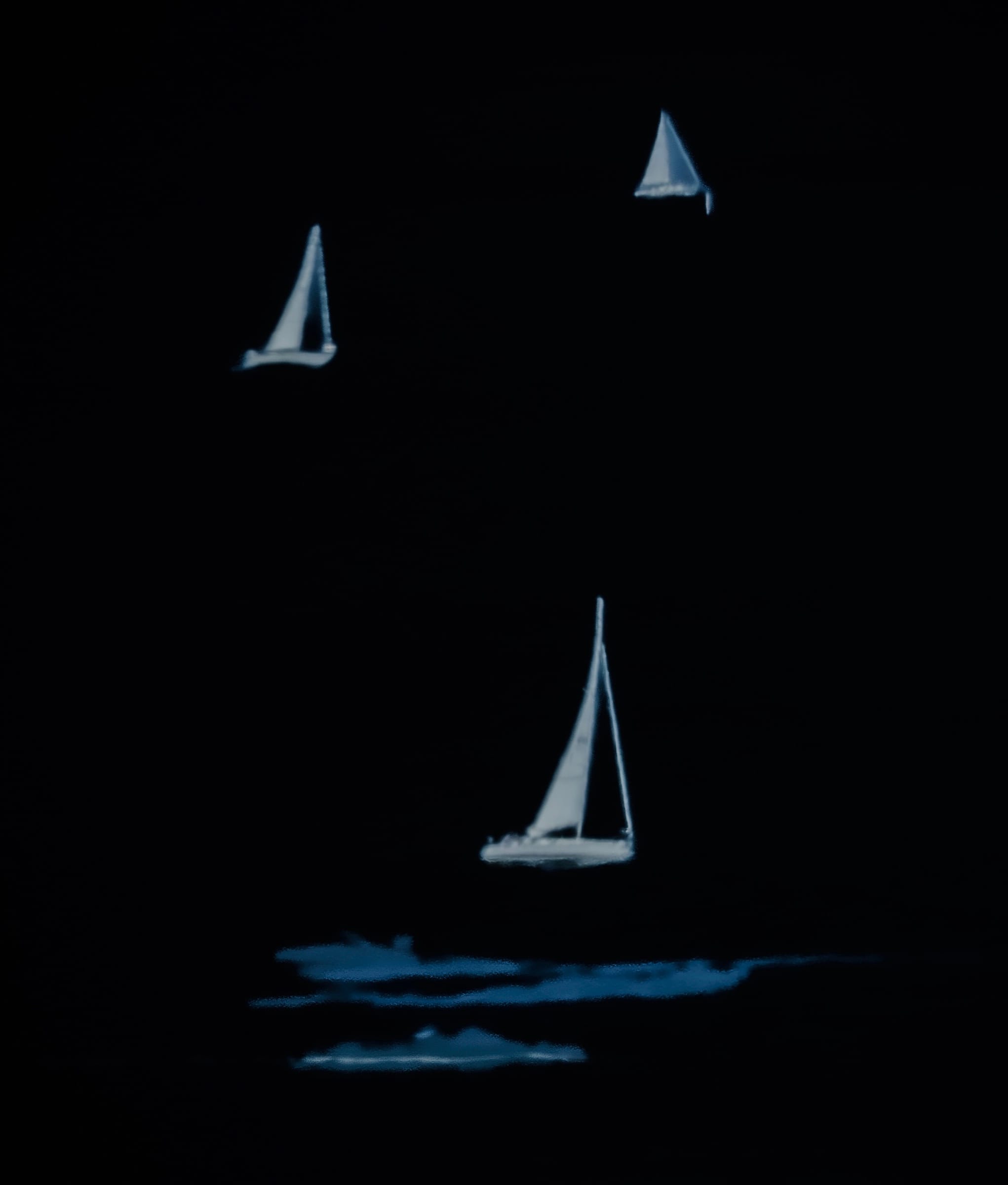 Three pale sailboats emerging from darkness above blue reflections