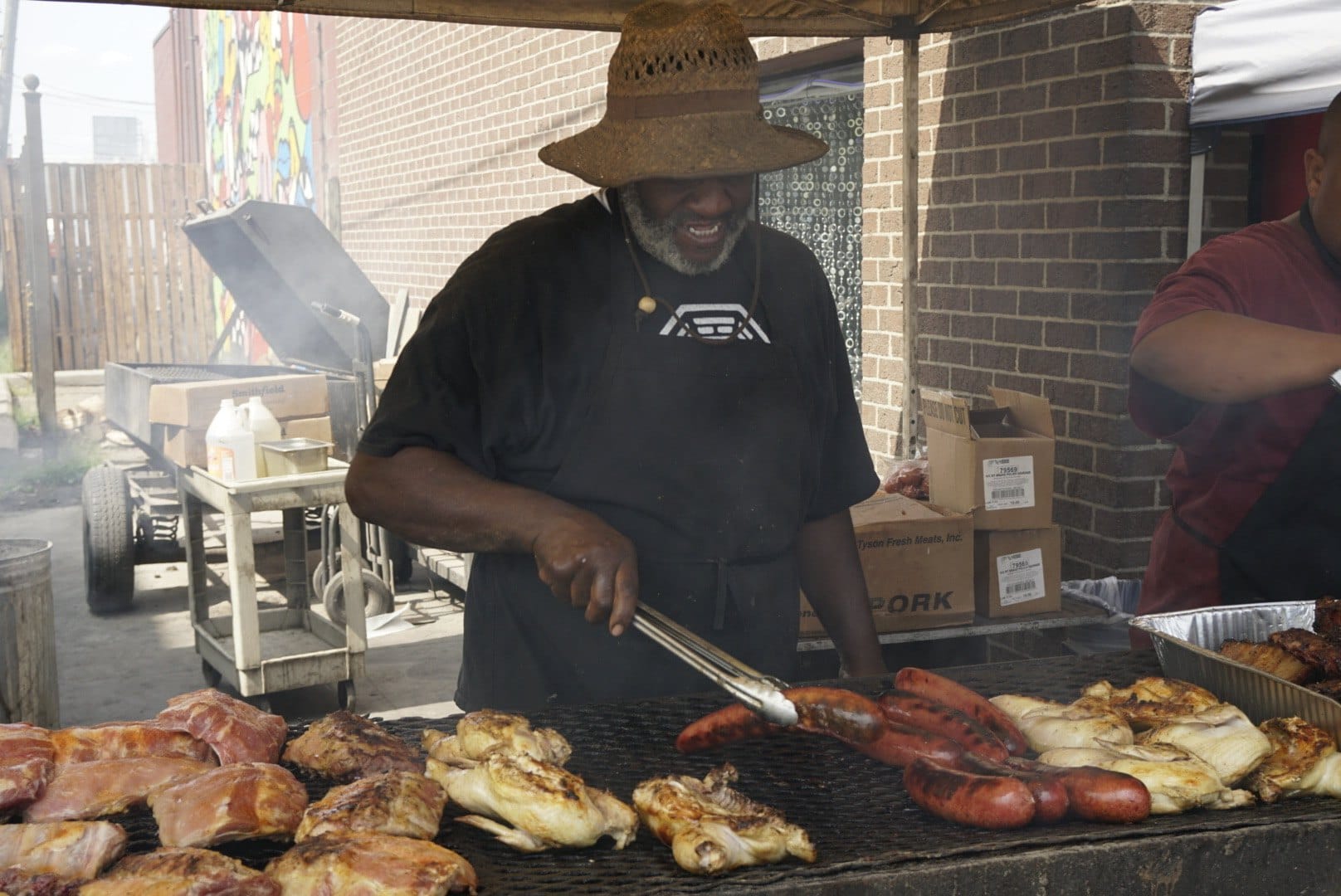 A food vendor grilling sausages at an outdoor market. — by Ed Shpritz