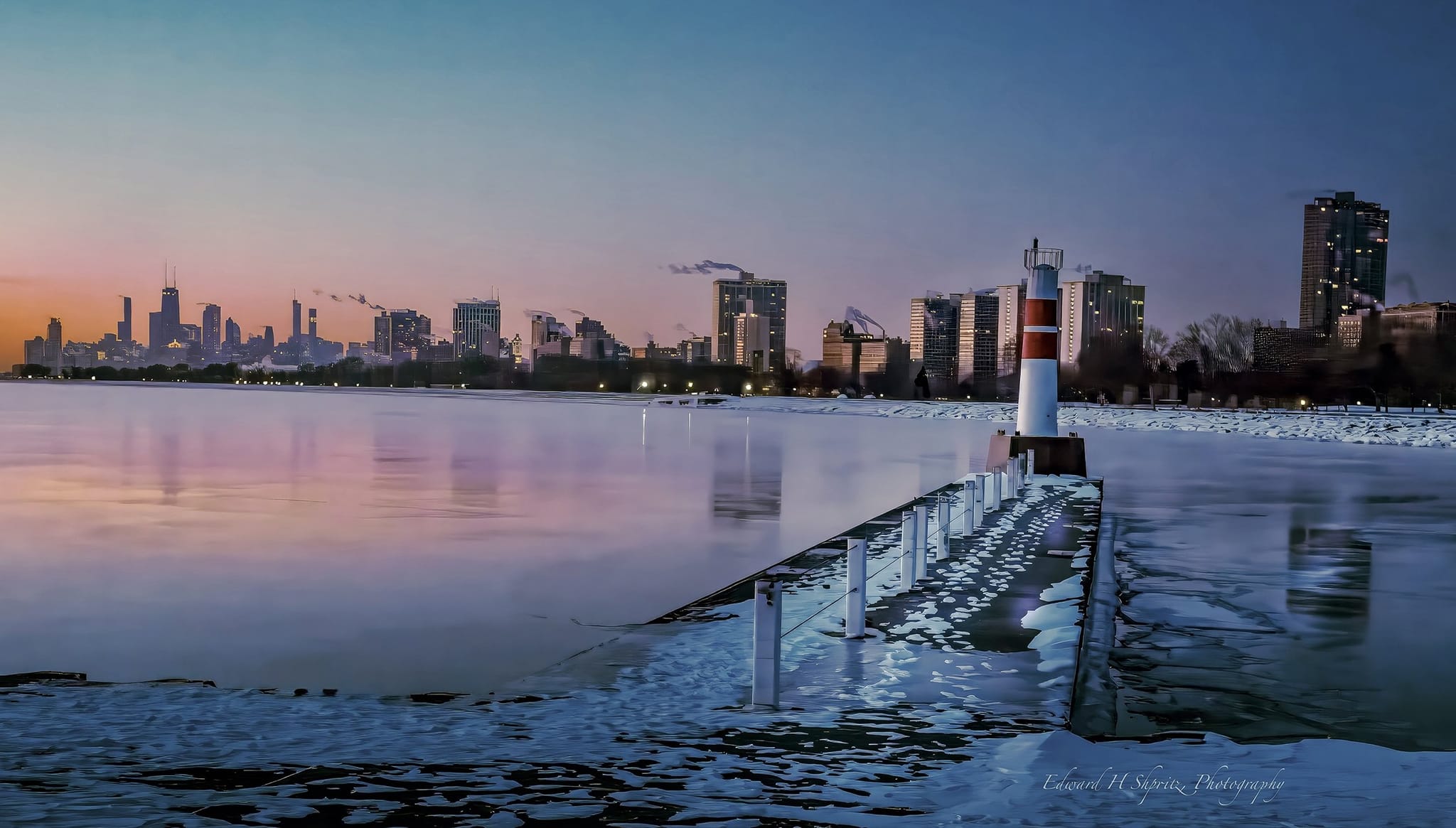 The Chicago skyline and a harbor light reflected in icy blue water at dawn