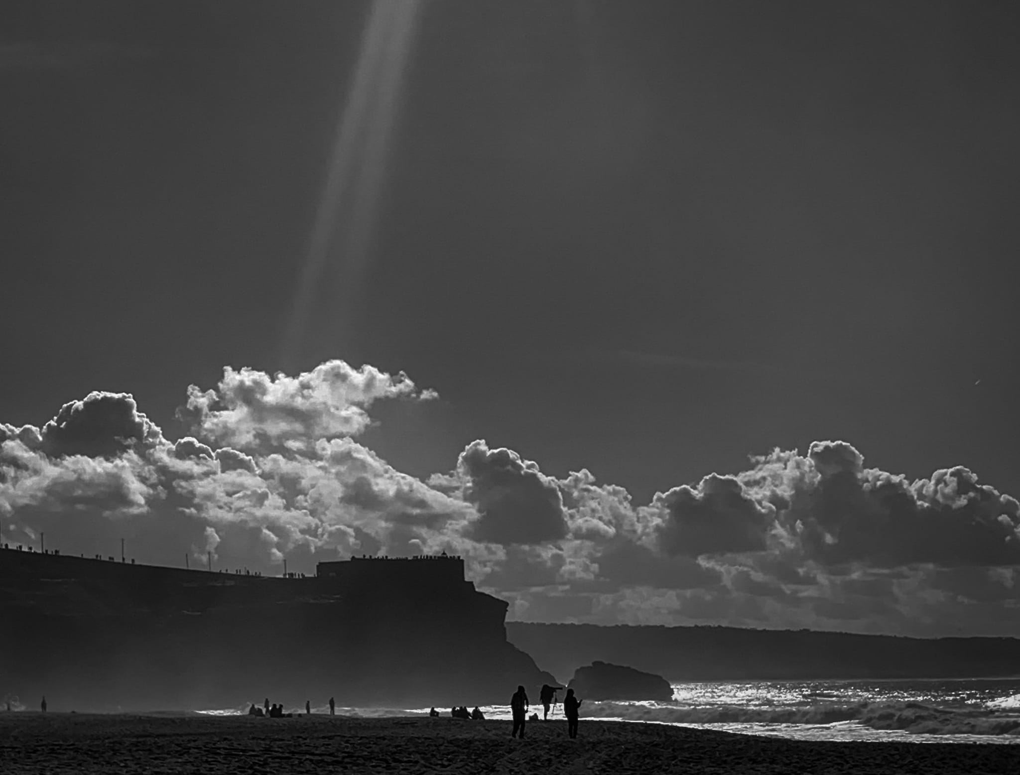 Sunbeams breaking through clouds above a shoreline in black and white