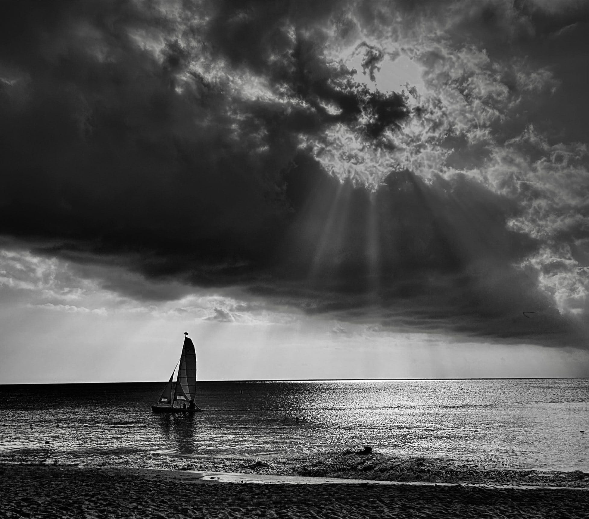 A lone sailboat beneath shafts of light breaking through a storm over the lake