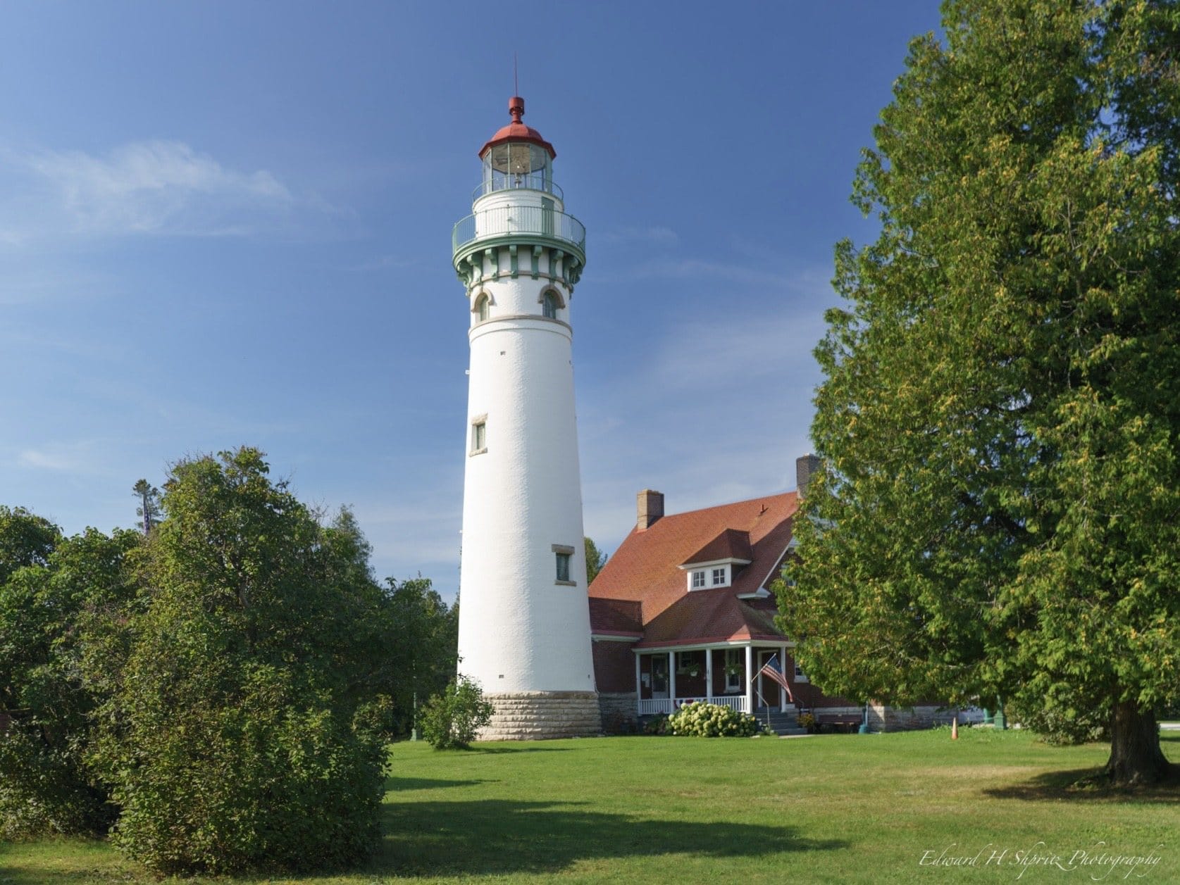 A white lighthouse rising above a green lawn beneath a clear blue sky