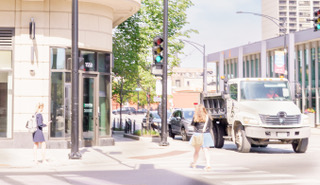 A woman crossing a bright city street corner with a truck at the light, high key pastel