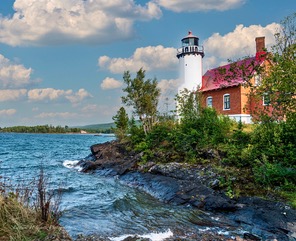 A lighthouse with a red roof on a rocky point above blue water
