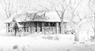 A snow covered log cabin among bare winter trees, high key white